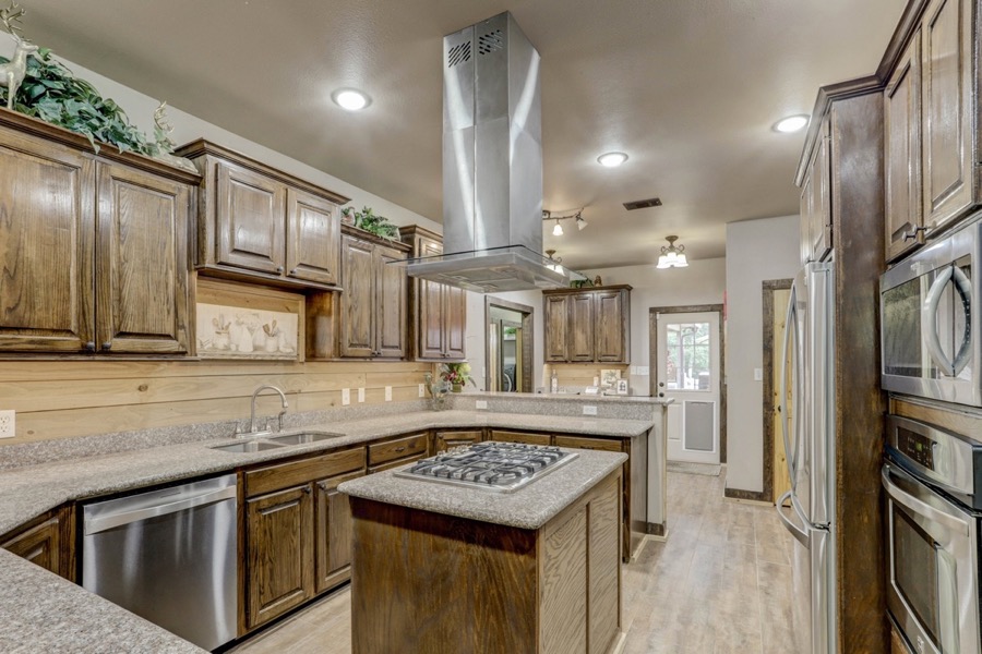 Inspira Ranch Casa Principal kitchen with center island, professional range hood, and dark wood cabinetry — Livingston TX