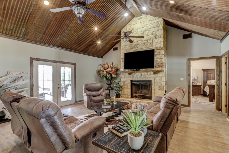 Inspira Ranch great room with floor-to-ceiling stone fireplace, vaulted corrugated-tin ceiling, and leather seating